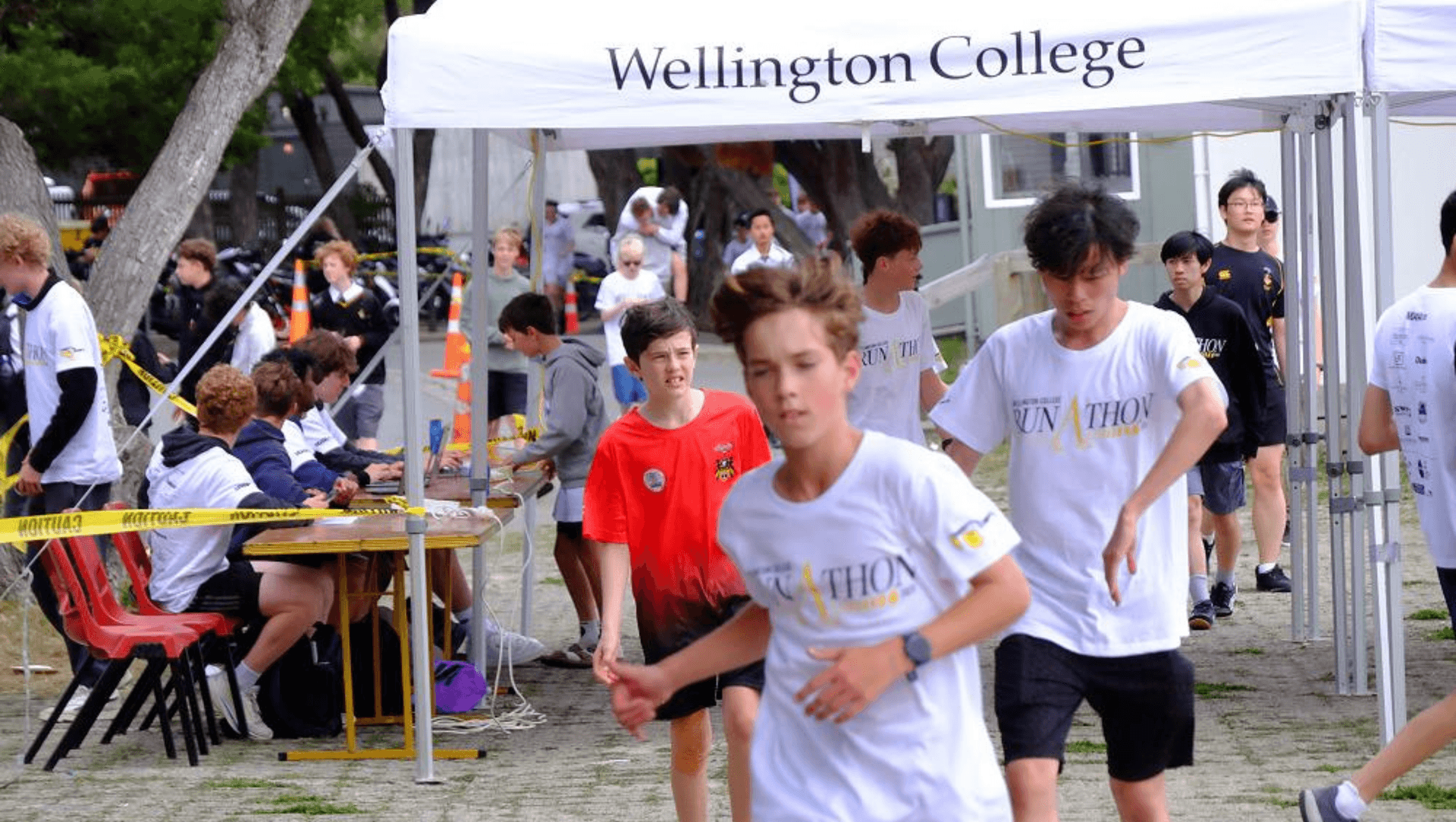 Participants running past a Wellington College tent during a marathon, with others seated nearby
